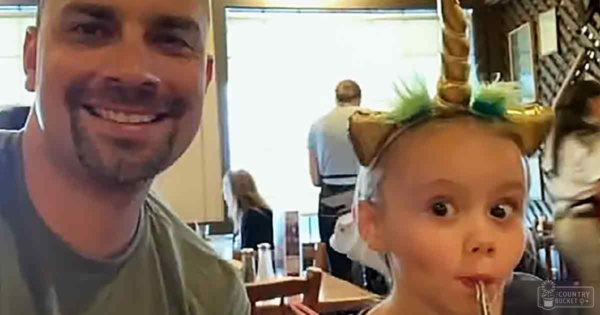 A toddler wearing a unicorn headband in an indoor restaurant setting with wooden chairs and condiments on tables, natural light suggesting spring or summer.