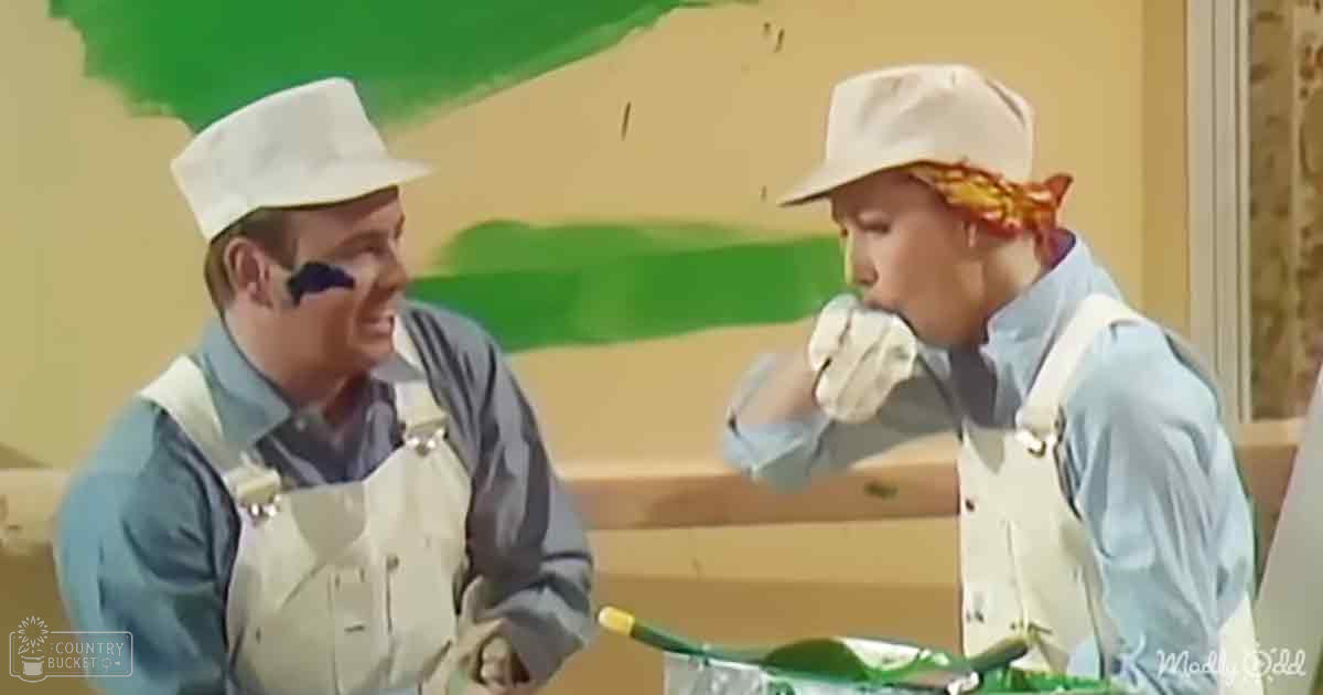 Two adults engaged in conversation, likely during a construction or renovation project; light blue button-up shirt with rolled-up sleeves and overalls on one adult, light blue long-sleeve shirt and white hat with red markings on the other. Setting appears to be indoors, possibly under renovation.