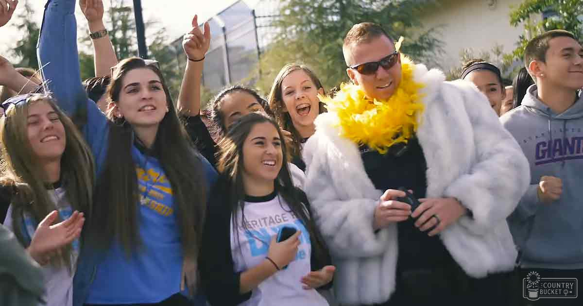 A group of young adults at an outdoor event, with a child wearing a light-colored jacket and others in casual attire, surrounded by trees and greenery under daytime spring or summer light.