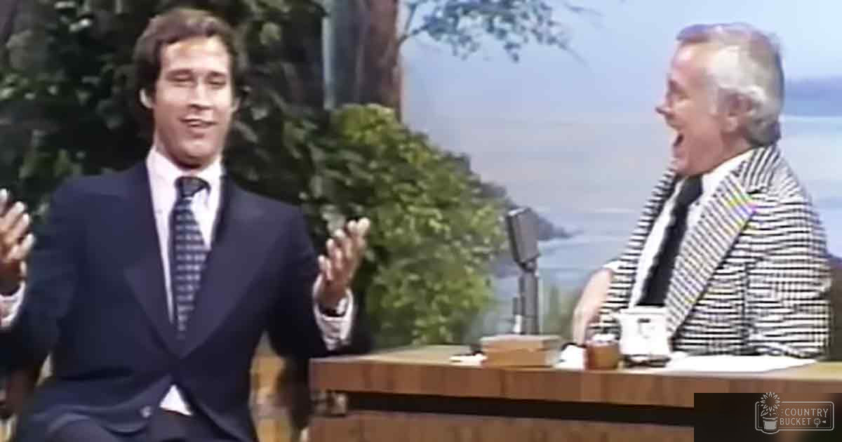 Young adult male in a dark suit jacket and tie, older adult male in a striped blazer and tie, interview setting with greenery and cityscape backdrop on an indoor studio set.