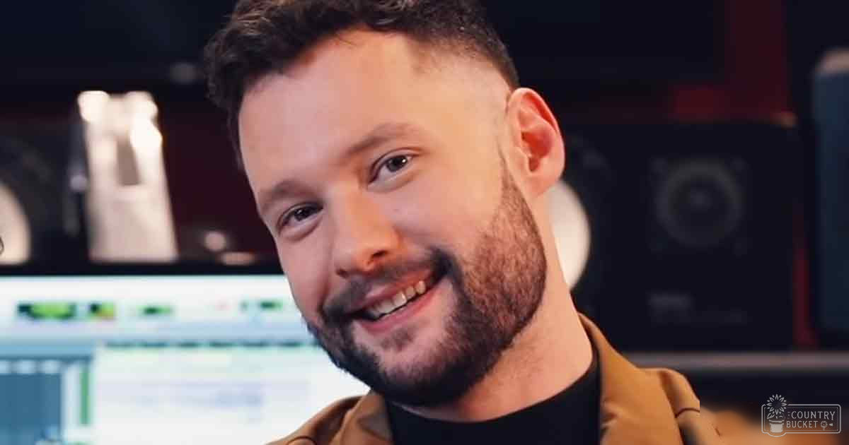 Young adult male in a modern casual style brown leather or faux leather jacket with a black turtleneck underneath stands indoors, possibly in a professional recording studio environment.