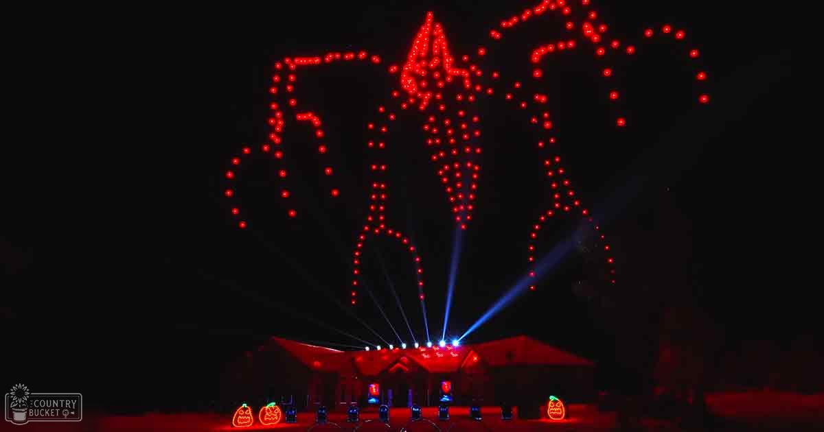 A house adorned with Halloween decorations illuminated by red lights at night, with beams of blue light projected upwards from its roofline.