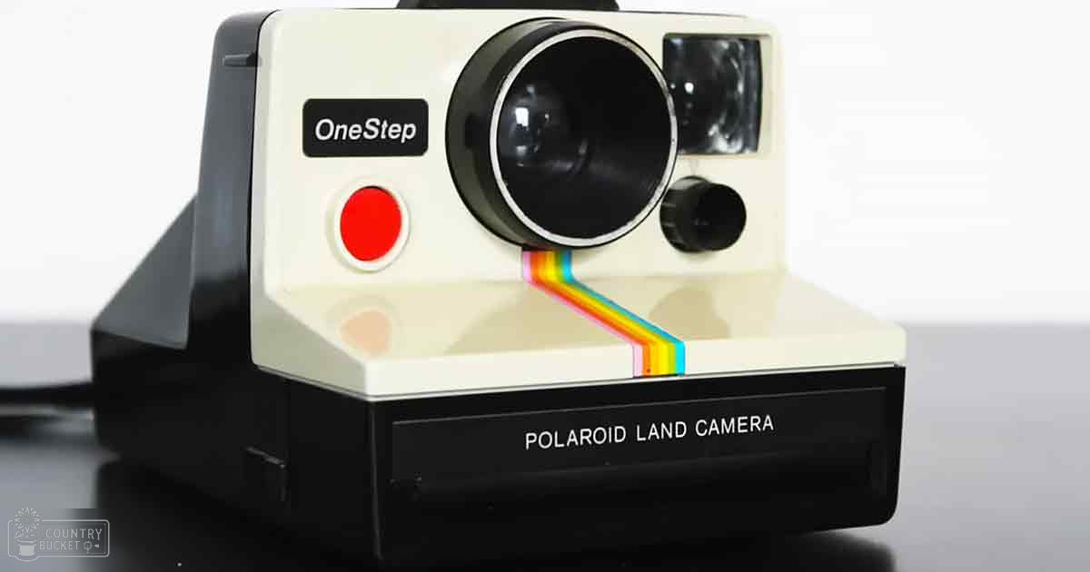 A Polaroid Land Camera OneStep with a white body, black accents, and a red 'OneStep' button sits on an indoor surface against a light background.