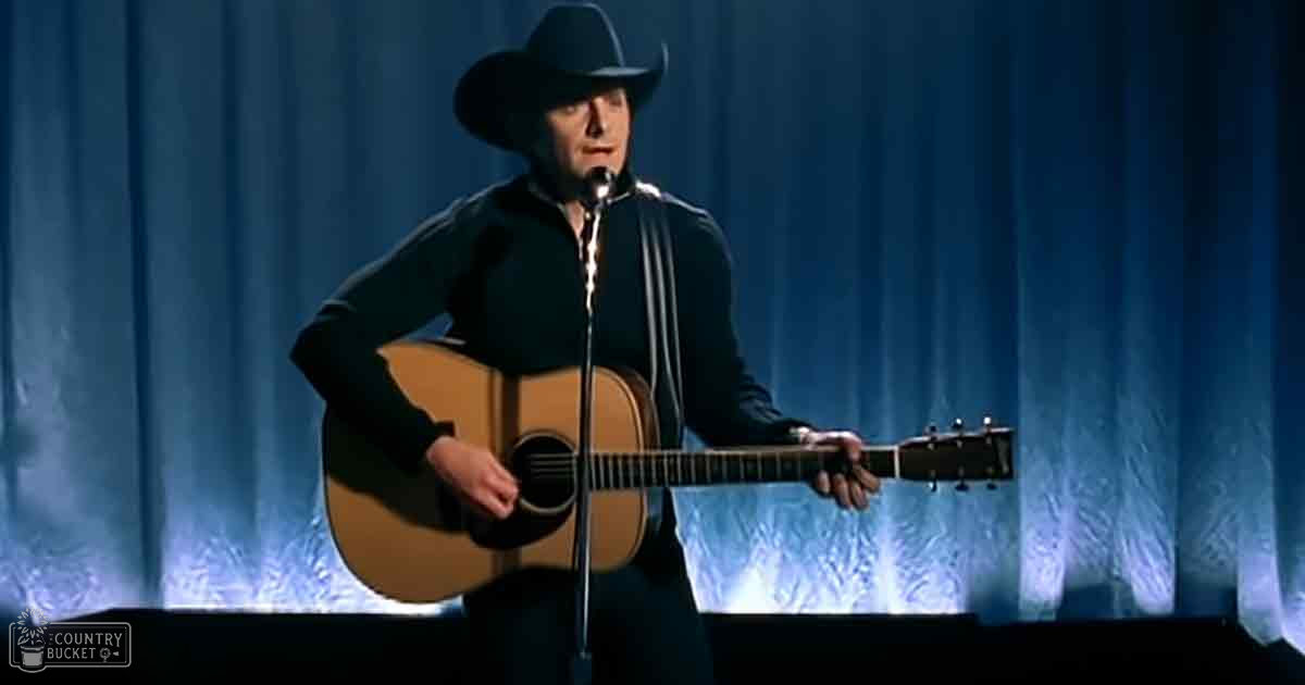 A middle-aged to older adult male singer in a country or western style, wearing a black long-sleeved shirt and wide-brimmed hat, performing on stage with an acoustic guitar.