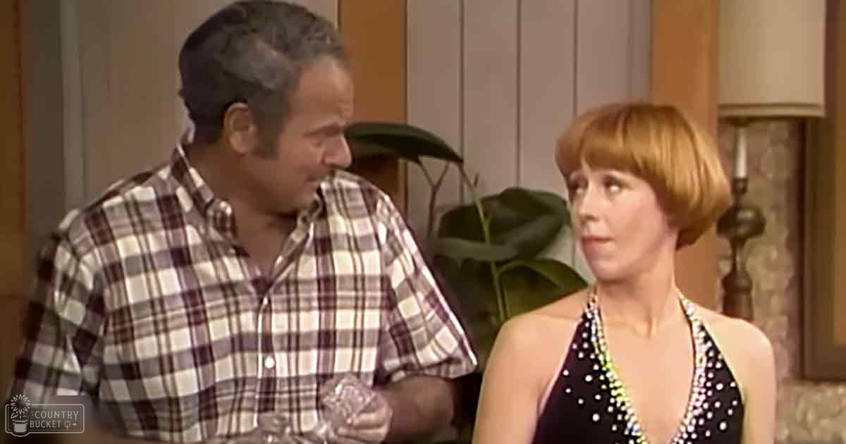 Middle-aged man wearing a plaid button-up shirt in a home setting alongside an adult woman in a black sequined dress, natural light streaming through.