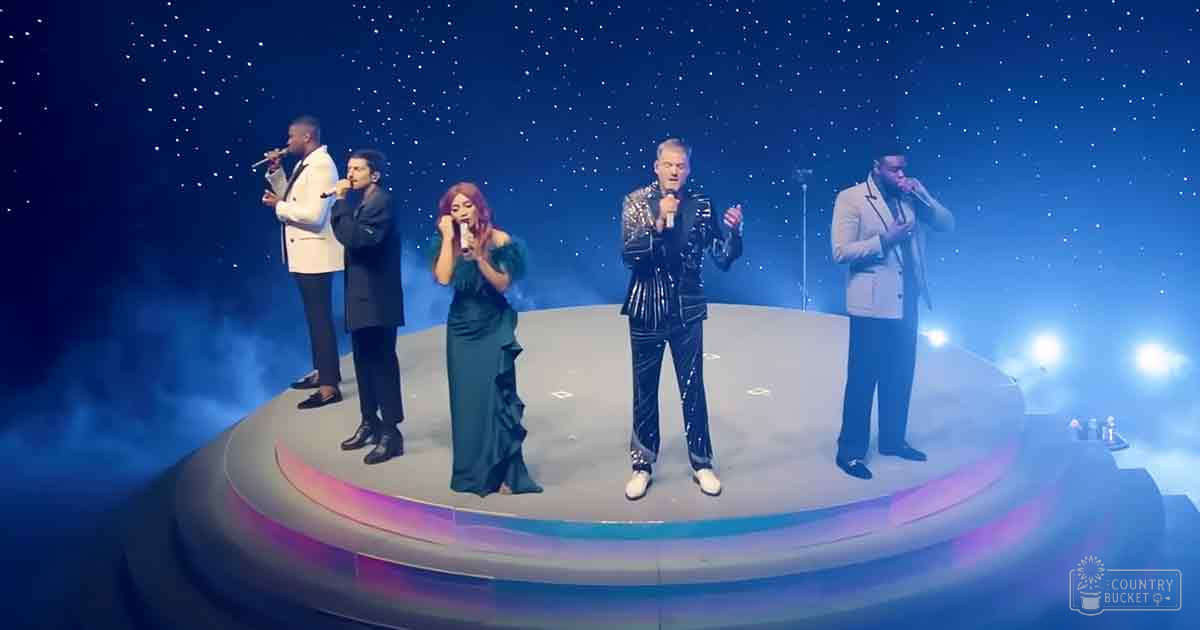 Musical performance group on stage in a concert setting, with adults wearing formal attire under blue-toned starry night sky effects.