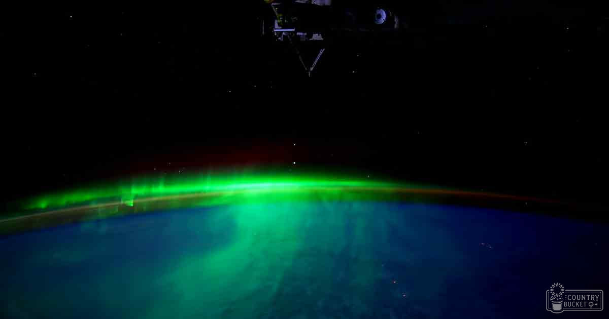 Aurora borealis over Earth with a spacecraft visible in space at night or early morning, showing stars and illuminated Earth.