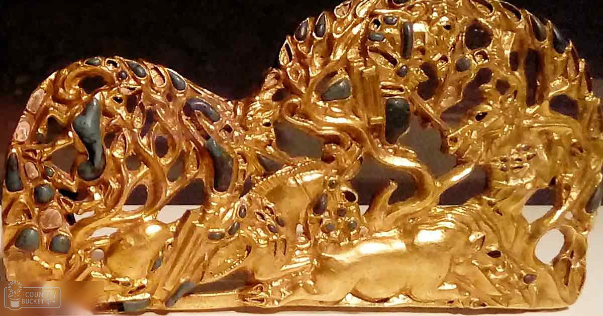 Close-up view of a golden artifact with intricate designs, possibly jewelry or ceremonial attire, set against a dark background.