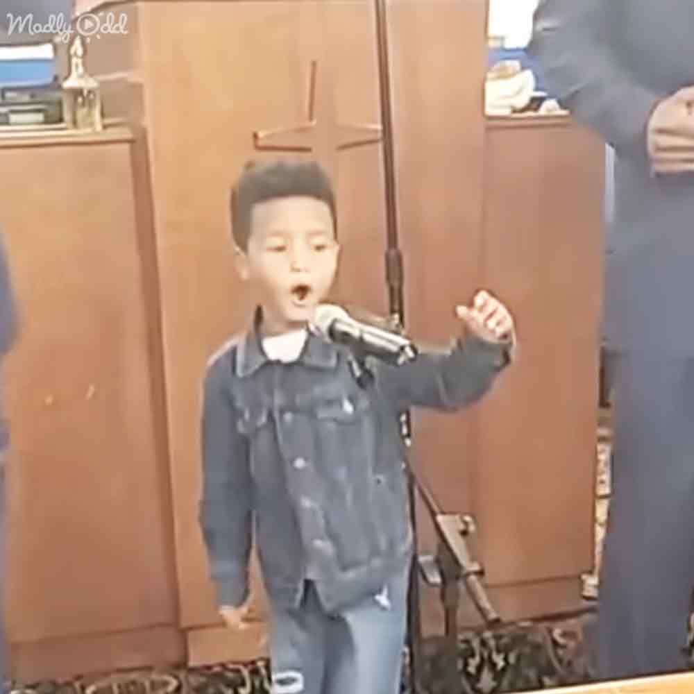 A child singing into a microphone in what appears to be a church setting during the daytime with even natural light.