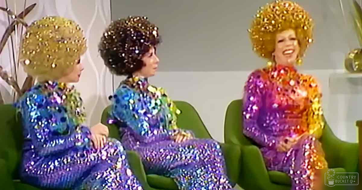Three adult female performers in a studio setting, each wearing vibrant sequined dresses with reflective patterns and colorful hues.