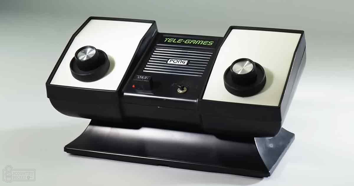 A vintage Atari Tele-Games Pong console with black and white color scheme, green text reading "TELE-GAMES" and "PONG," and the Atari logo visible against a plain white surface and neutral gray backdrop.