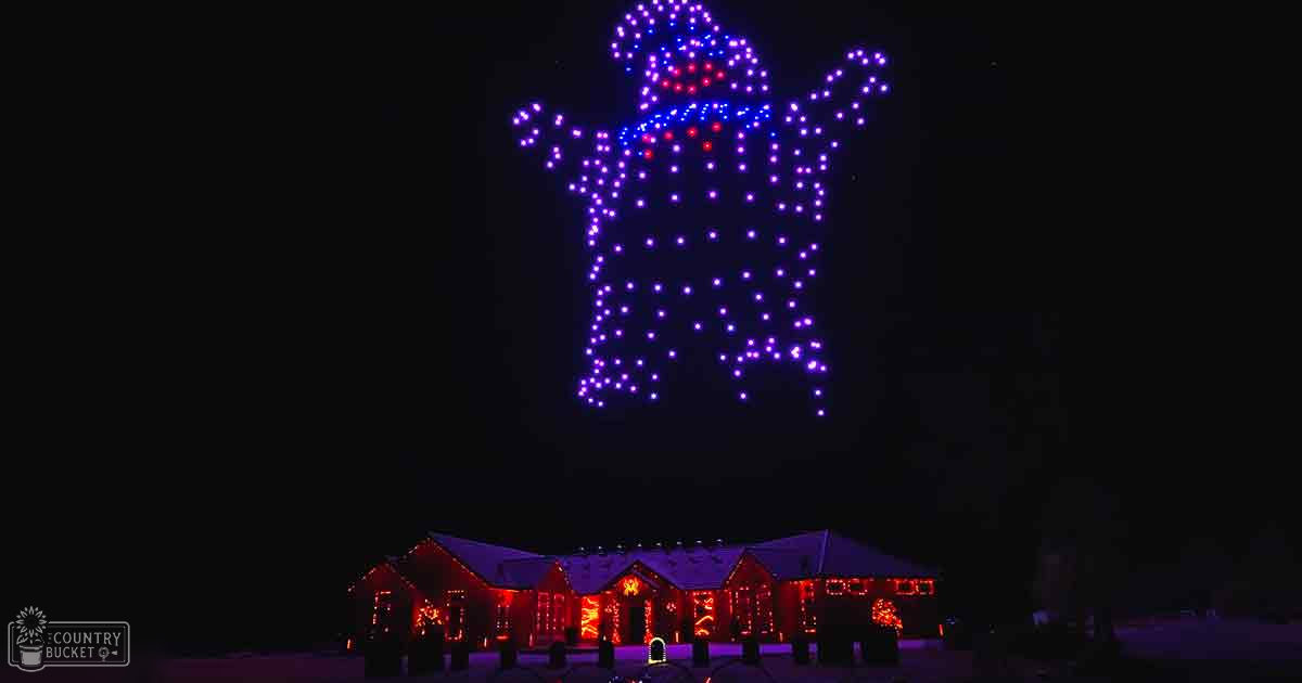 Drone light show forming a character shape over a residential area adorned with red and white holiday lights at nighttime, snow-covered ground visible in winter setting.