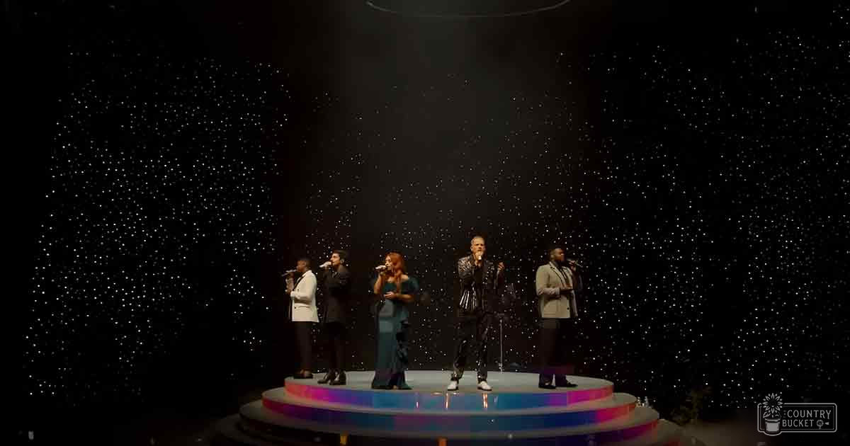 An indoor stage setting with a musical performance group in formal attire during what appears to be an evening event under artificial lighting.
