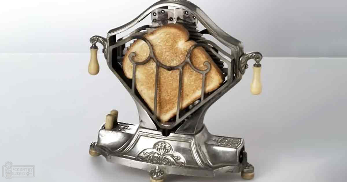A vintage-style toaster with intricate scrollwork, two slices of toasted bread inside, set against a plain white background in what appears to be a studio setting.