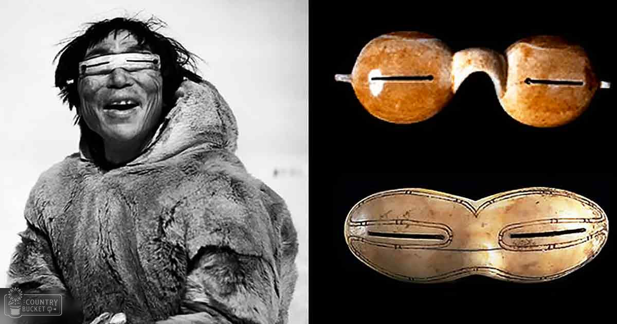 An older adult male wearing a traditional Arctic fur parka in a snowy outdoor setting with two ancient-looking eye masks as focal objects.