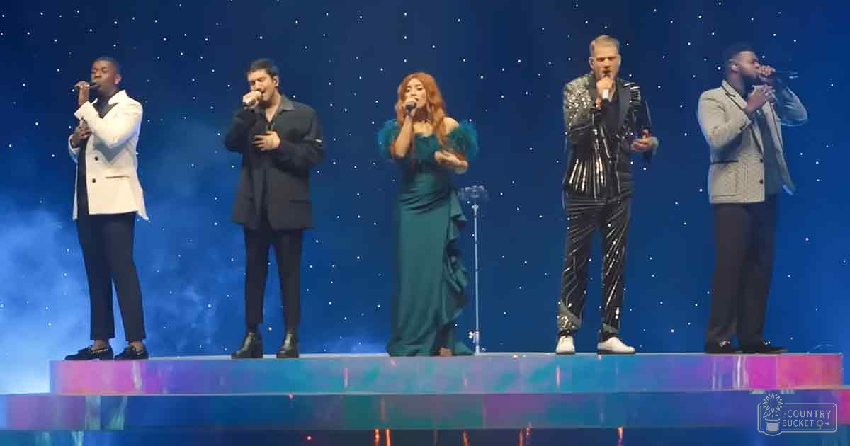 A performance group with young adult to middle-aged individuals dressed in formal attire on an indoor stage against a starry backdrop at night.