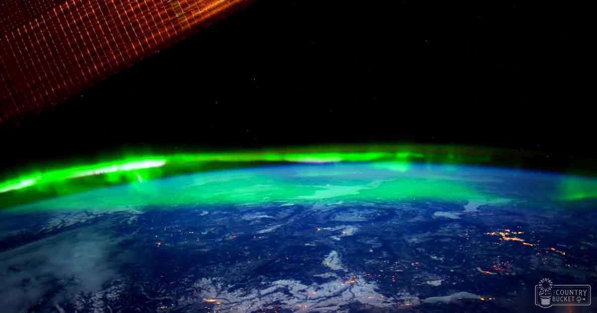 A view of Earth from space at night with visible green auroras and illuminated city lights.