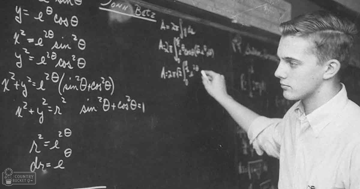 A young adult male wearing a mid-20th-century short-sleeved button-up shirt in front of a chalkboard filled with mathematical equations, likely in an educational classroom setting during spring or summer.