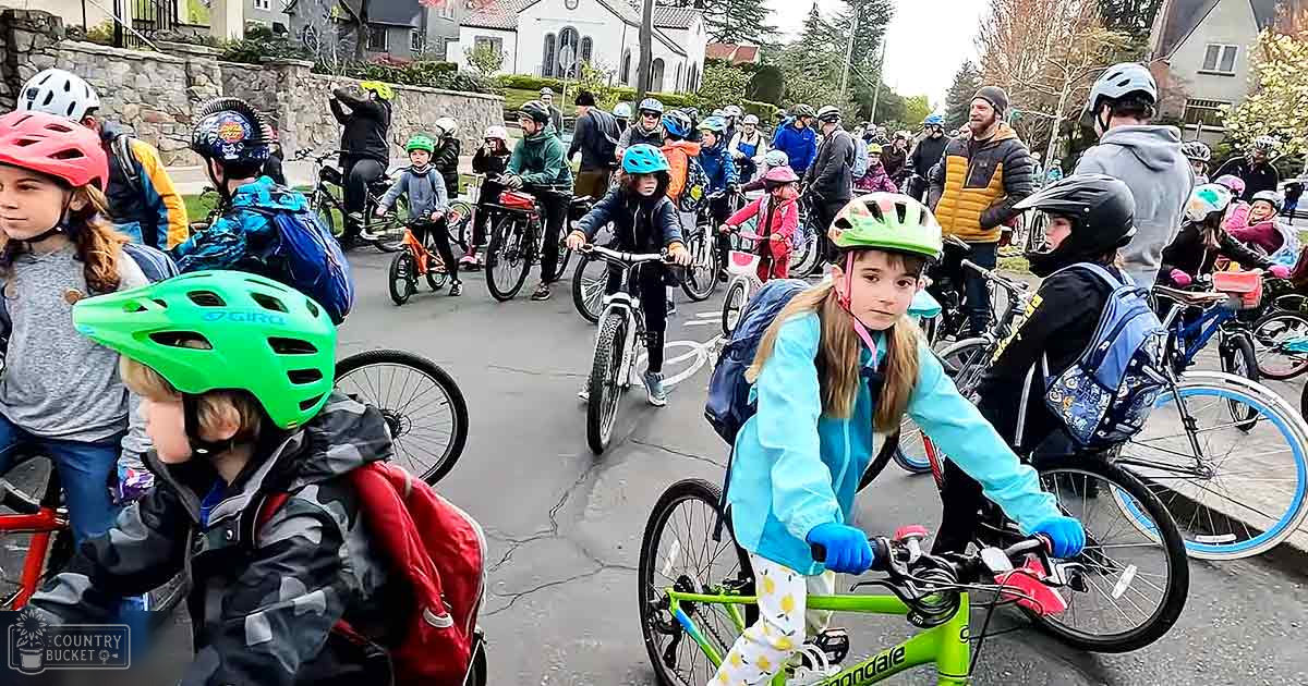 Children wearing helmets and jackets participate in a bike ride along a residential street on a sunny day.