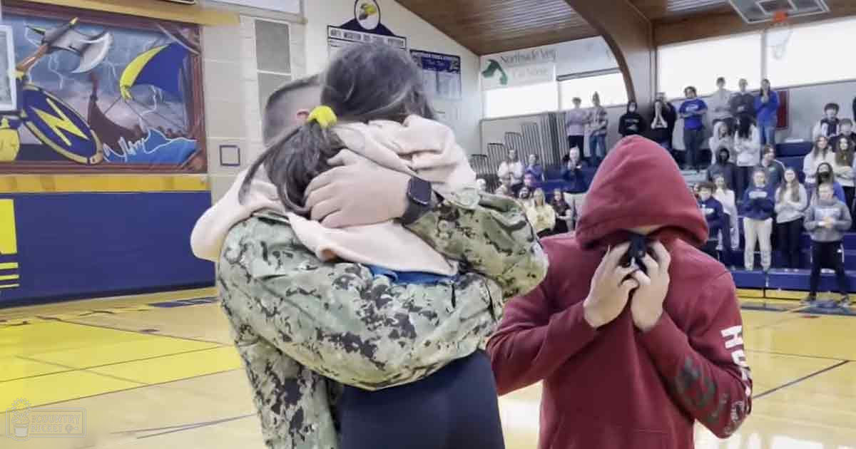 A soldier hugging a child at an indoor school gymnasium during what appears to be a homecoming or reunion event.