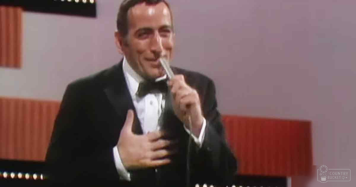 A formal adult male in an indoor setting, wearing a black tuxedo with white shirt and bow tie, holding an award or trophy.