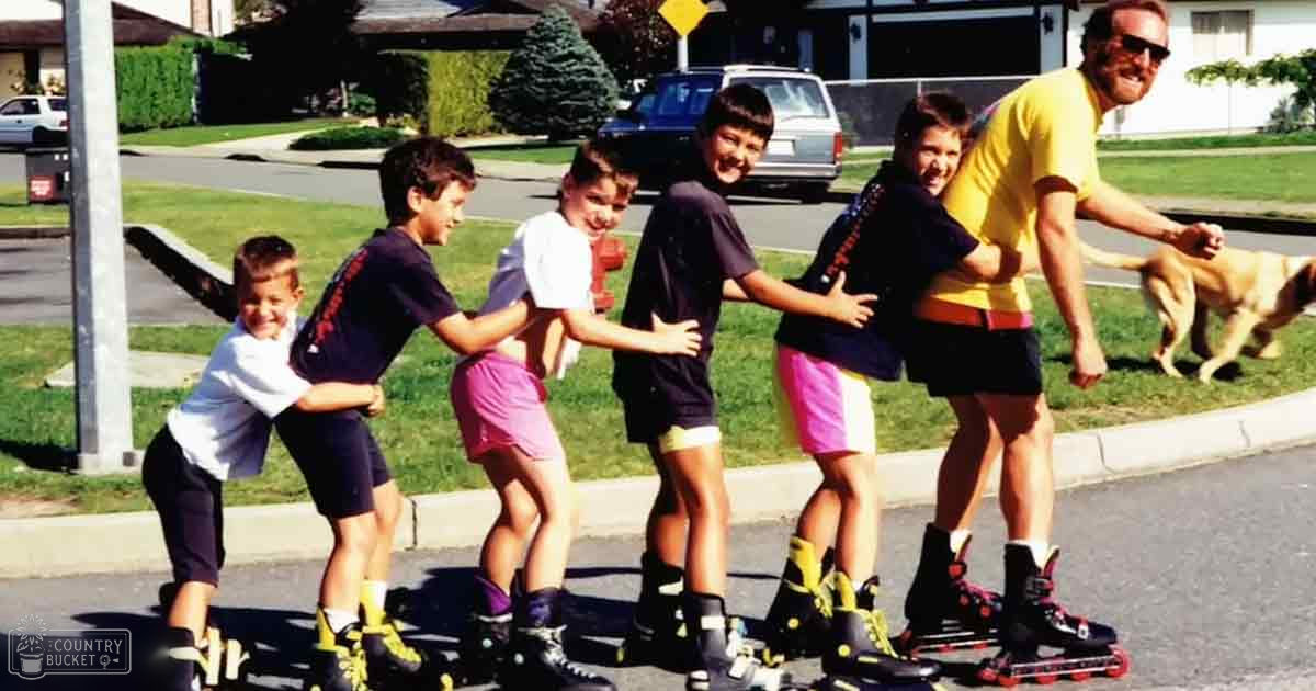 Group of children rollerblading with an adult in a suburban neighborhood, golden retriever dog nearby; spring or summer setting, greenery abundant.