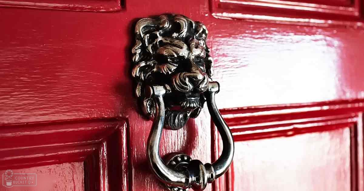 A close-up of a silver lion's head door knocker attached to a glossy red wooden door with paneling, indoors.