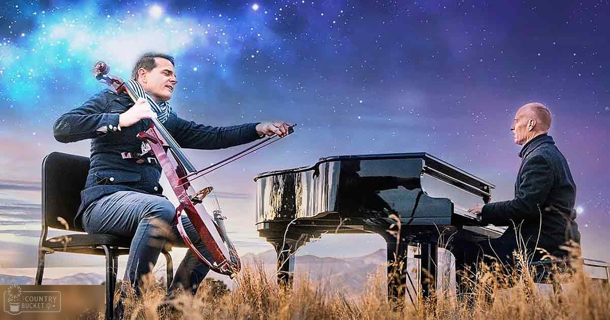 Duet of musicians playing cello and piano in an open field under a starry sky with mountains in the background during dusk or dawn.