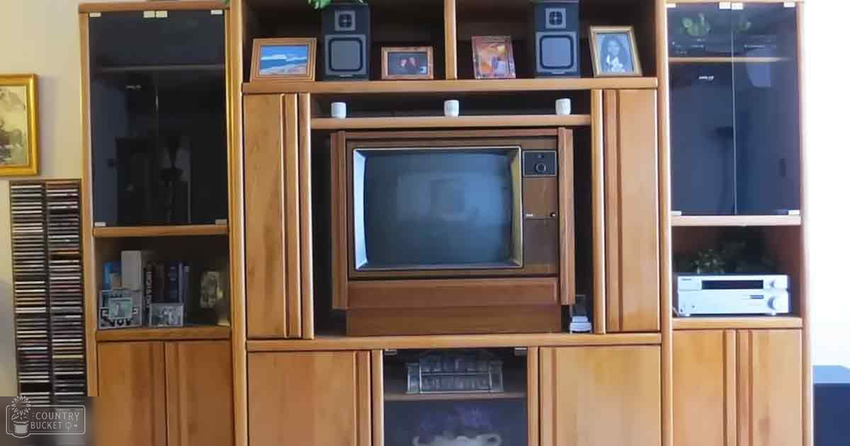 An old CRT television in a wooden entertainment center with framed photos and CDs, likely indoors in a living room setting.