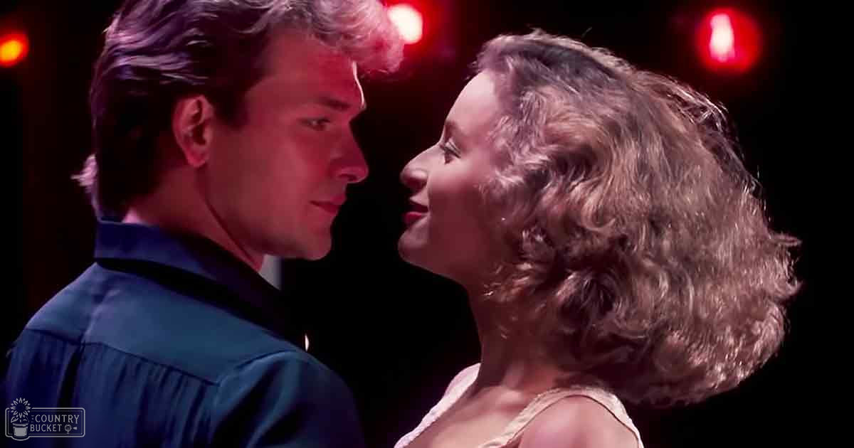 A young adult male and female couple performing an intimate dance or dance scene under dim red stage lighting, wearing casual and elegant attire respectively.