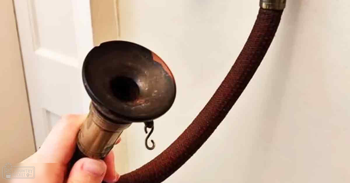 Close-up of a hand holding a vintage smoking pipe with dark mouthpiece and brown hose, set against plain white walls in an indoor home environment.