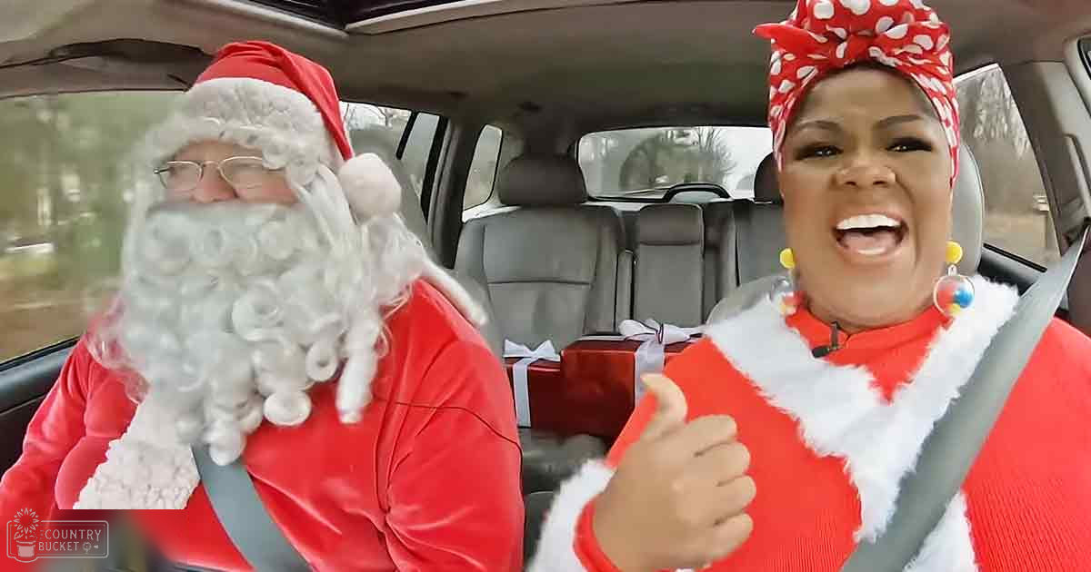 A car interior with two individuals dressed in festive attire, possibly during Christmas time; older adult male wearing a classic Santa Claus costume and female adult in a red holiday sweater with white fur trim.