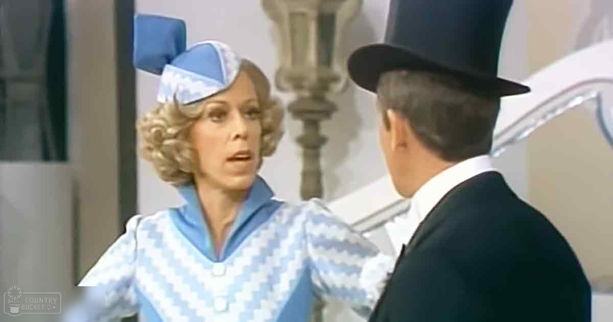 A middle-aged woman in a flared-sleeve blue and white checkered dress with a large bow on her head stands indoors near an ornate column. A man in a black suit jacket and top hat is partially visible to the side.