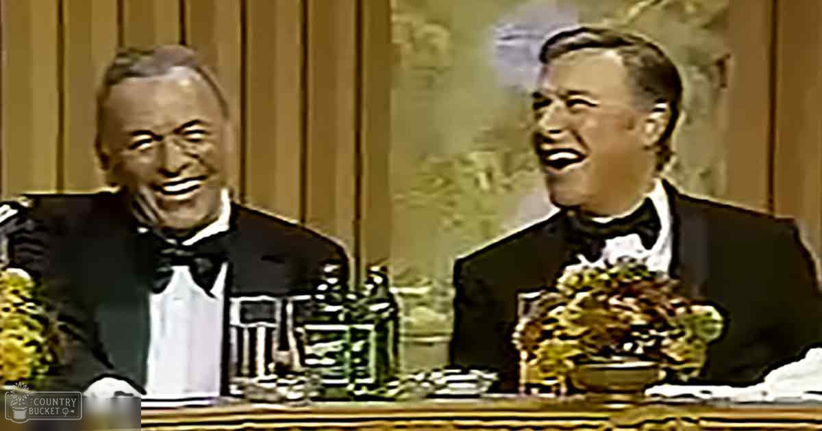 Middle-aged comedic duo performing in a studio setting with greenery and decorative bowls on a table behind them.