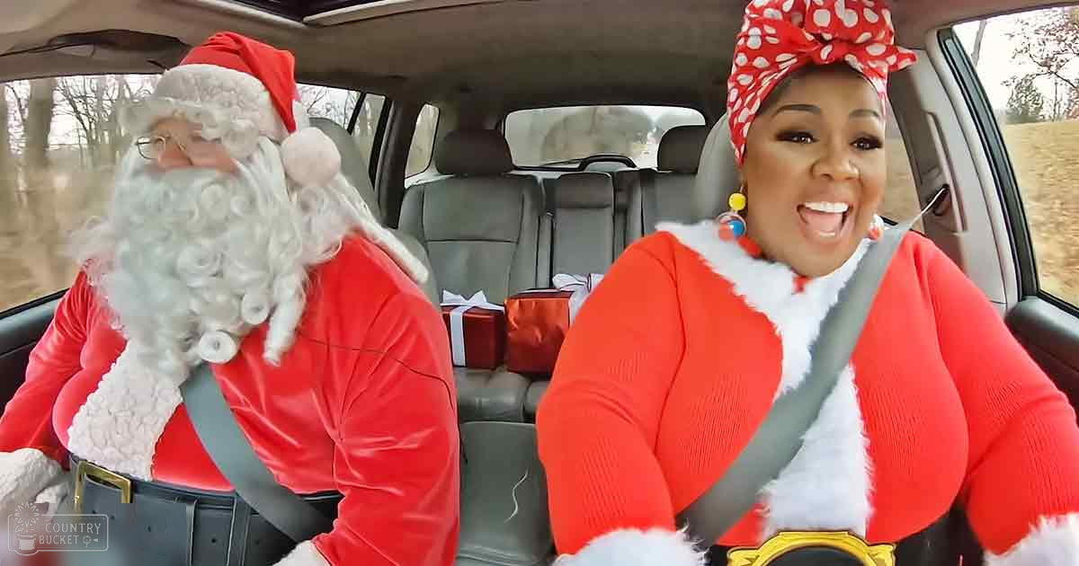 Outdoor winter scene with two adults dressed as Santa and Mrs. Claus, seated inside a car filled with wrapped presents.