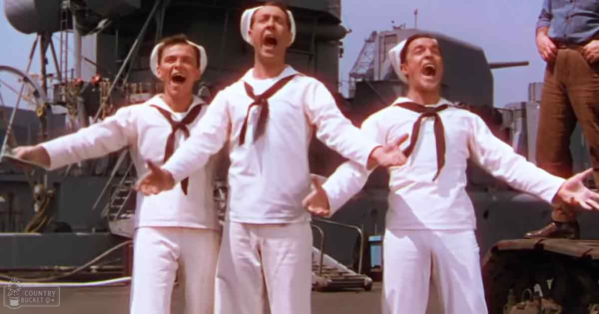 Young adult male sailors in white sailor suits with dark brown neckerchiefs singing on a naval ship during summer midday.