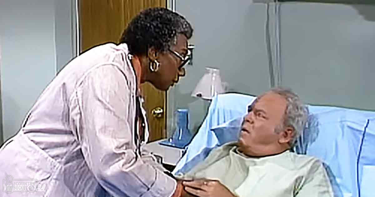 Healthcare professional wearing a white lab coat interacts with an older adult in a hospital room, clinical decor and bright lighting indicate daytime setting.