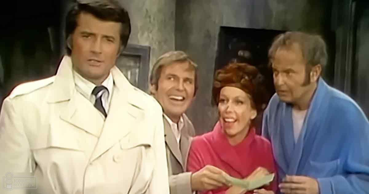 A group of four adults indoors, with a focus on their clothing: white trench coat with double-breasted front, light gray suit jacket, bright pink turtleneck sweater, and blue robe. The setting appears to be a room or studio with dark curtains and framed pictures.