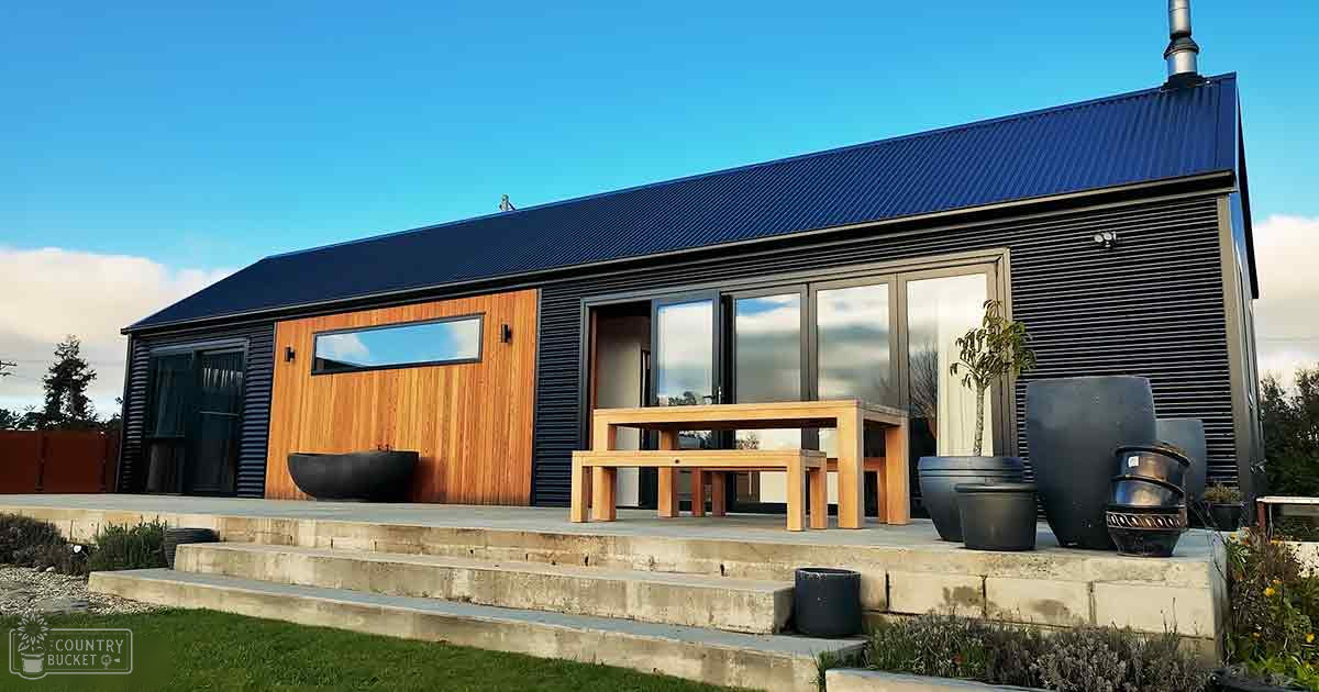 Modern house with large windows and wooden accents, situated in an outdoor residential area with clear blue skies and scattered clouds.