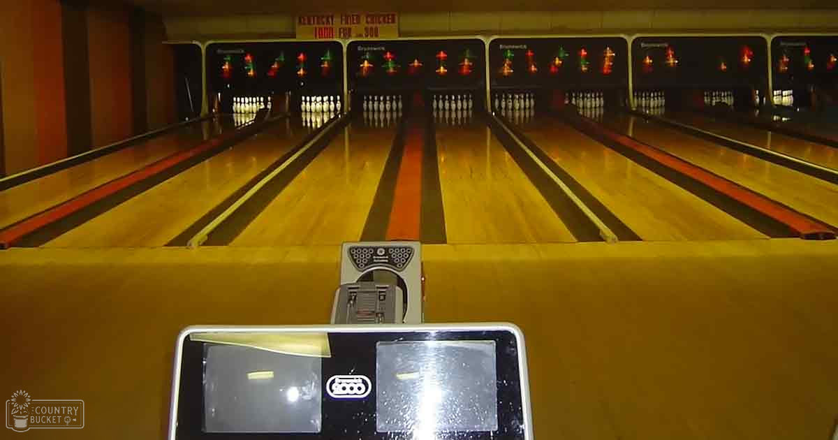 Indoor view of a bowling alley at night with artificial lighting illuminating the lanes and yellow and orange tones on the lane surface.