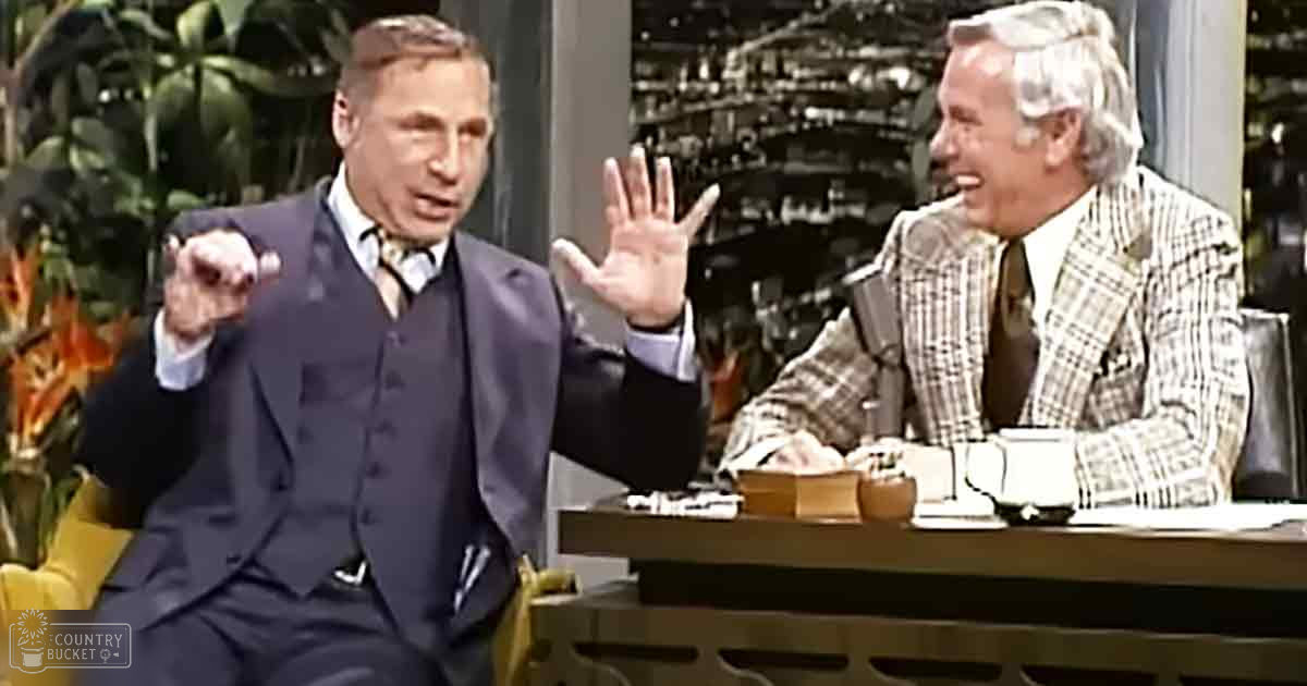 Two older adult men in a talk show setting with formal attire, dark wooden desk furniture, indoor backdrop suggesting daytime studio lights.