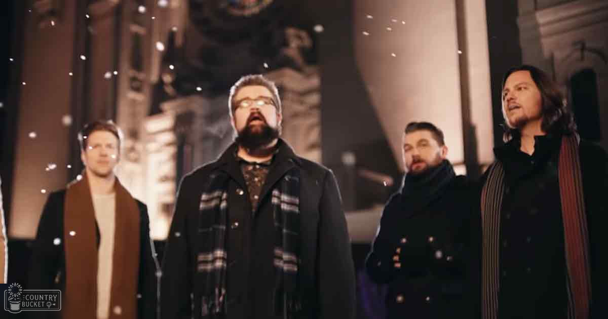 A group of men singing in front of an ornate building during winter, with muted browns and grays dominating the scene.