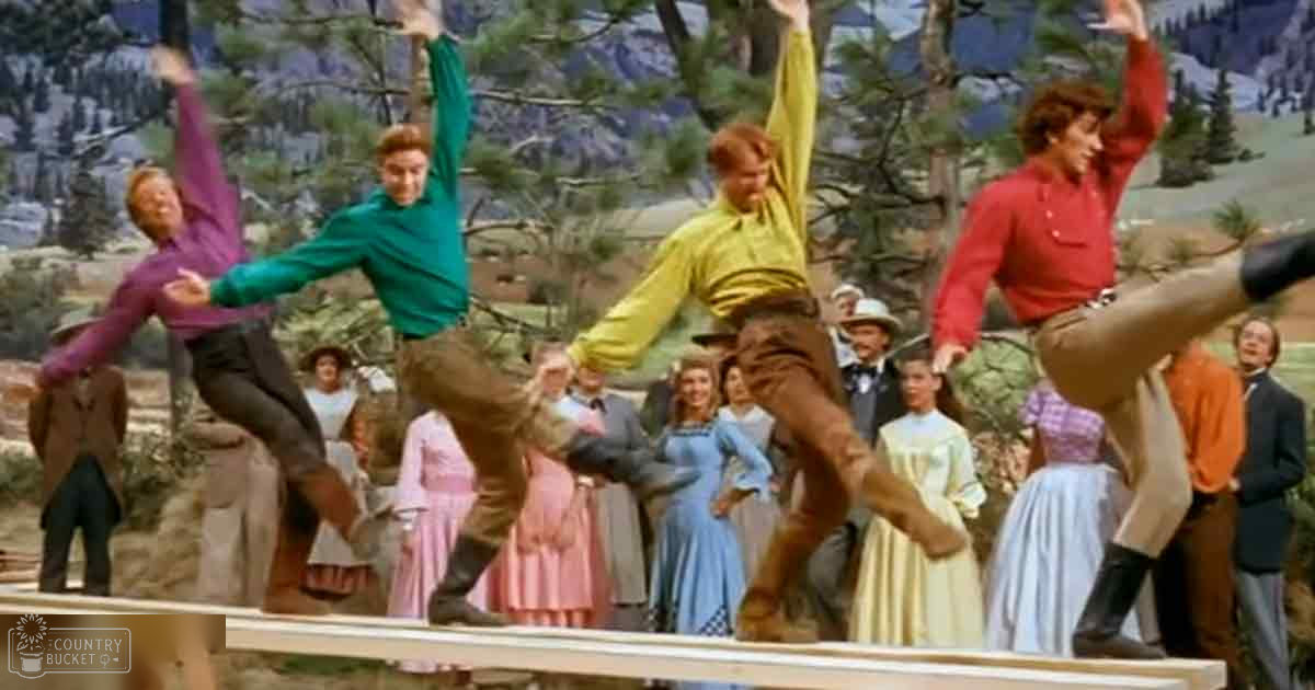 Group of young adult male dancers performing outdoors against a backdrop of a mountainous Western landscape with spring or summer vegetation under bright midday light.
