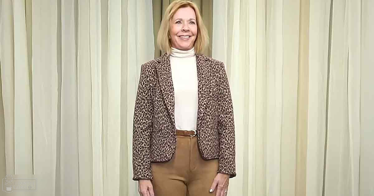 A middle-aged woman wearing a leopard print blazer and white turtleneck in an indoor setting.