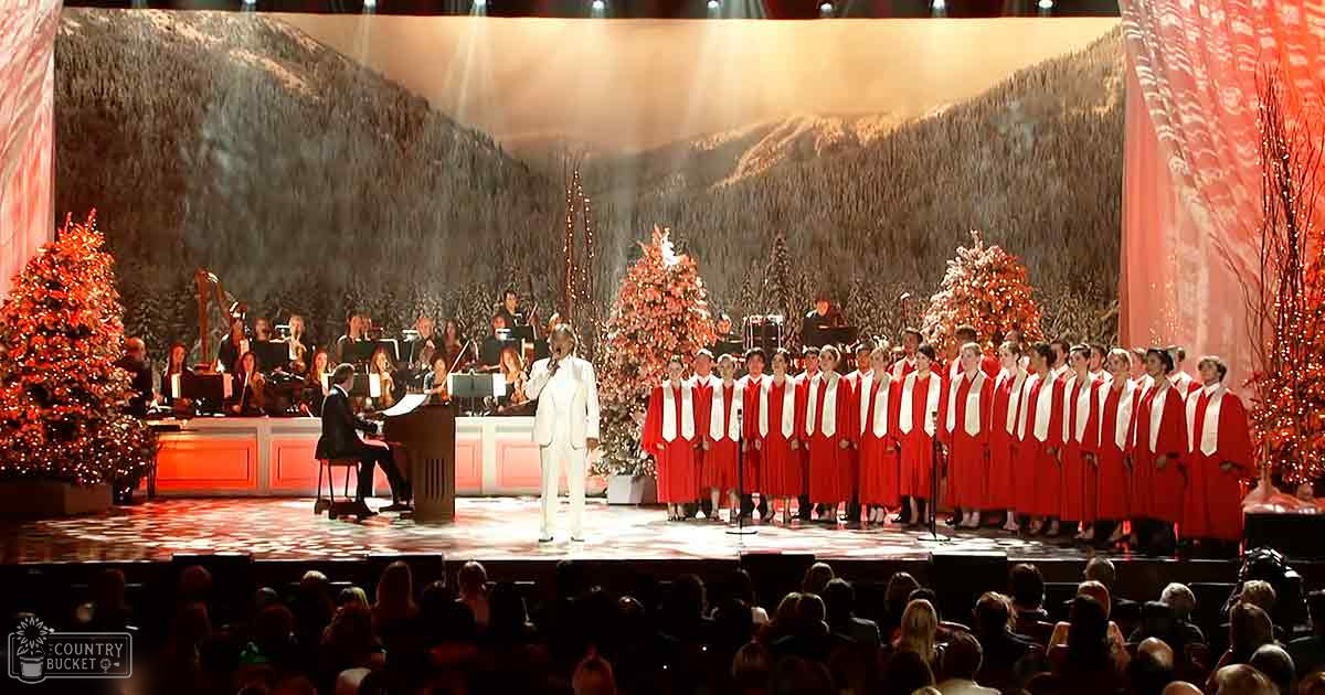 A choir performing in an auditorium with Christmas decorations and a snowy mountain backdrop during a winter-themed event.