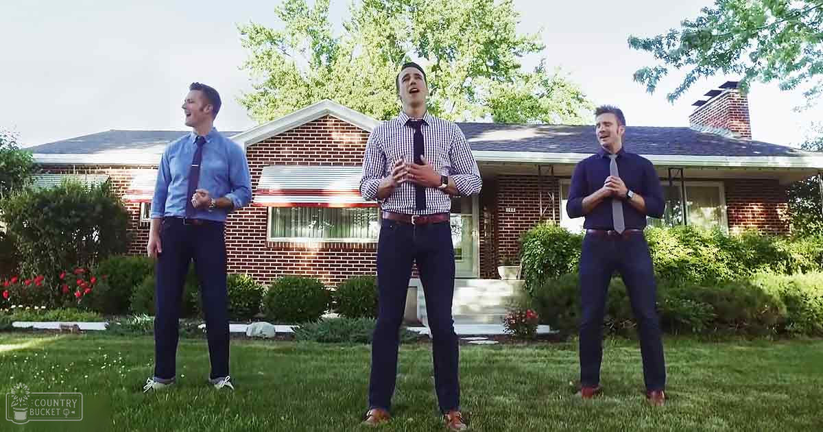 A group of young adult males singing outdoors in front of a suburban house on what appears to be a spring or summer day.