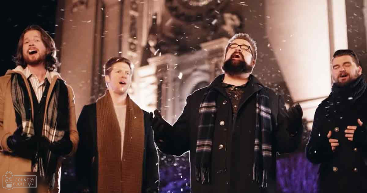 A group of adult men singing outdoors in front of an ornate building during winter at night.