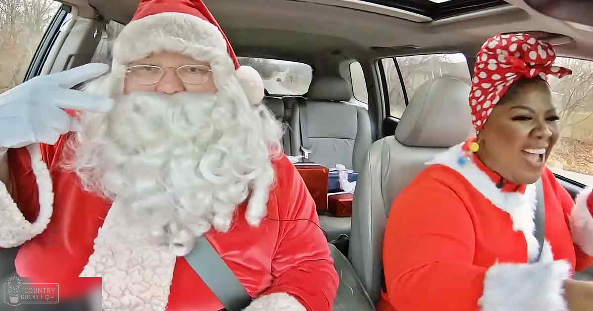 A man dressed as Santa Claus sits in a car with another festive individual beside him, both wearing holiday-themed attire.