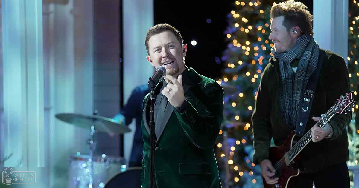 Musical performance with festive decorations indoors, with an adult male singer in a dark green velvet suit and another person holding an electric guitar.