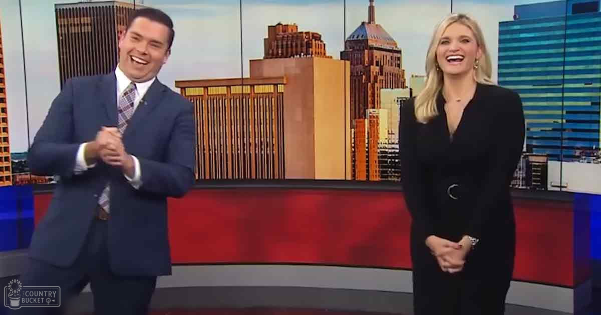A news broadcast set against a city skyline, with two adults in formal attire during daytime.